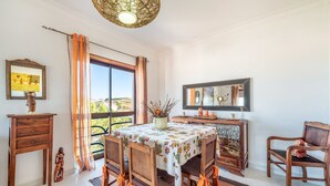 Un coin repas avec une table dressée pour quatre personnes, des chaises en bois, un buffet en bois, un grand miroir et une vue par la fenêtre.