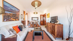Un salon comprenant un canapé, une table basse, un téléviseur, un meuble en bois et un coin repas avec des chaises et une table.