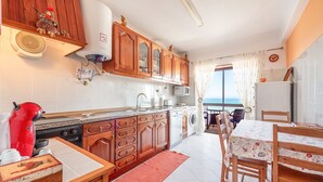 Une cuisine avec des meubles de rangement en bois, une bouilloire rouge et une vue sur la mer par la fenêtre.