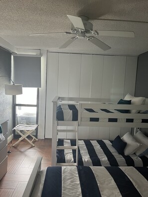 Cozy bedroom with a bunk bed arrangement, ceiling fan, and a window offering a view of the outside.