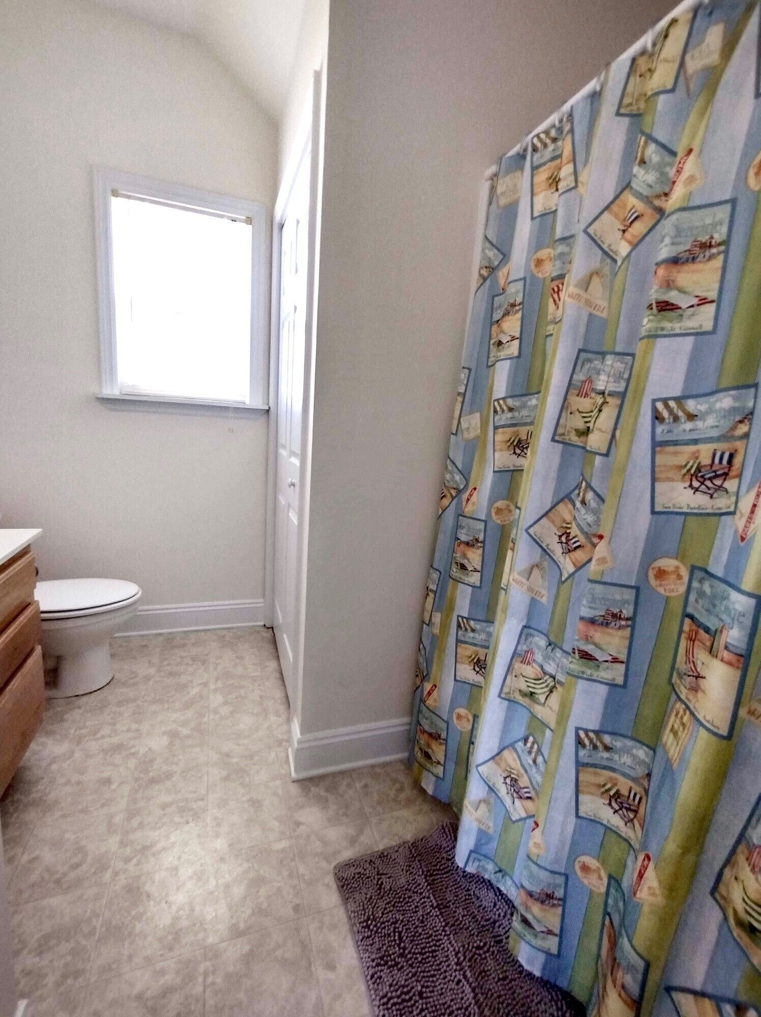 A bathroom with a toilet, a window, and a shower curtain with nautical prints.