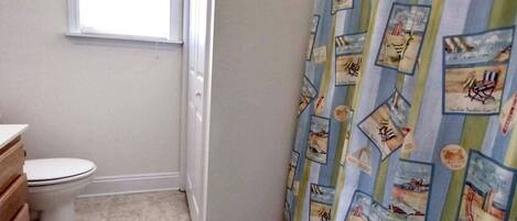 A bathroom with a toilet, a window, and a shower curtain with nautical prints.