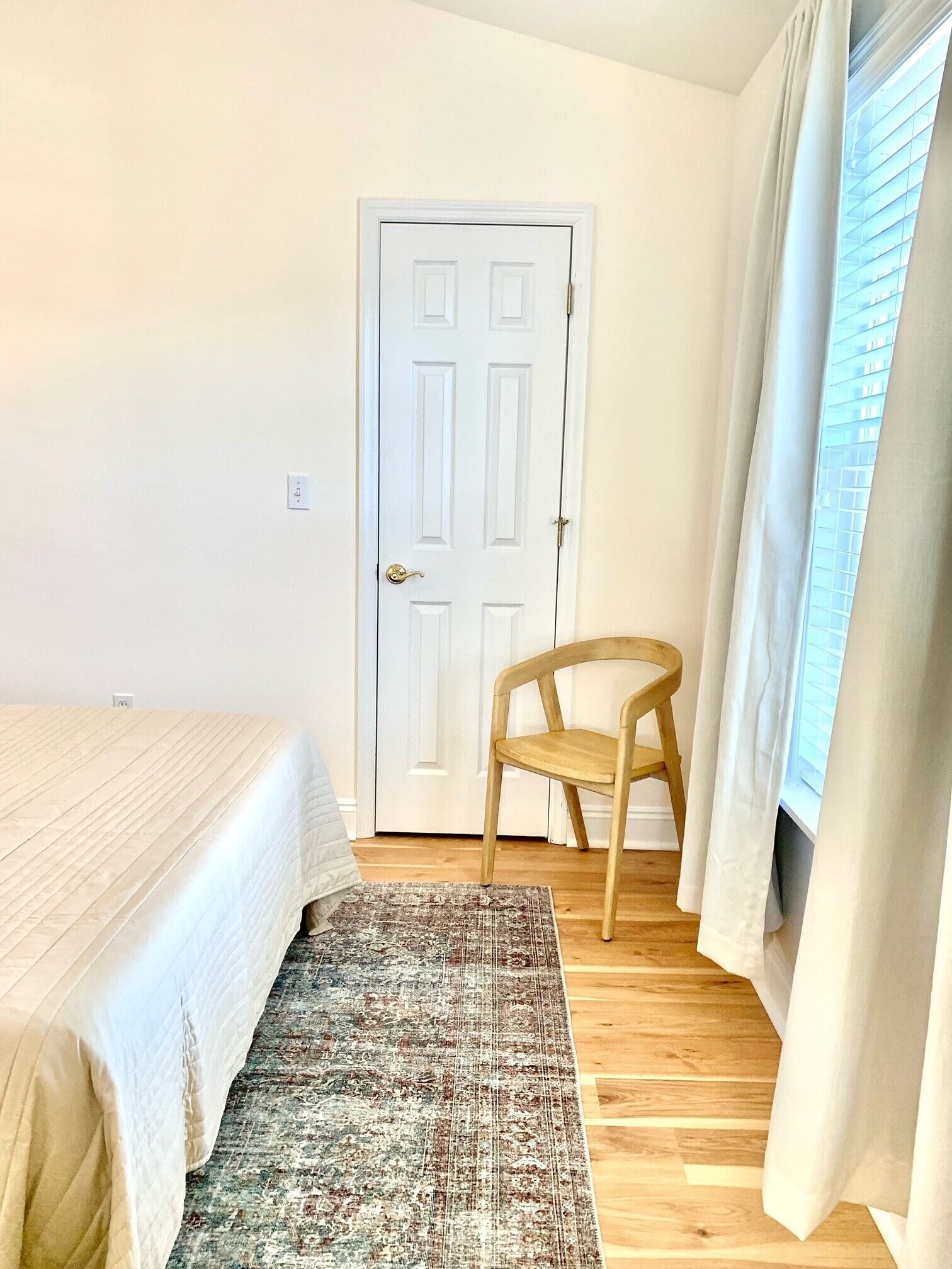 A bedroom with a bed, a chair, a door, and a window with curtains.