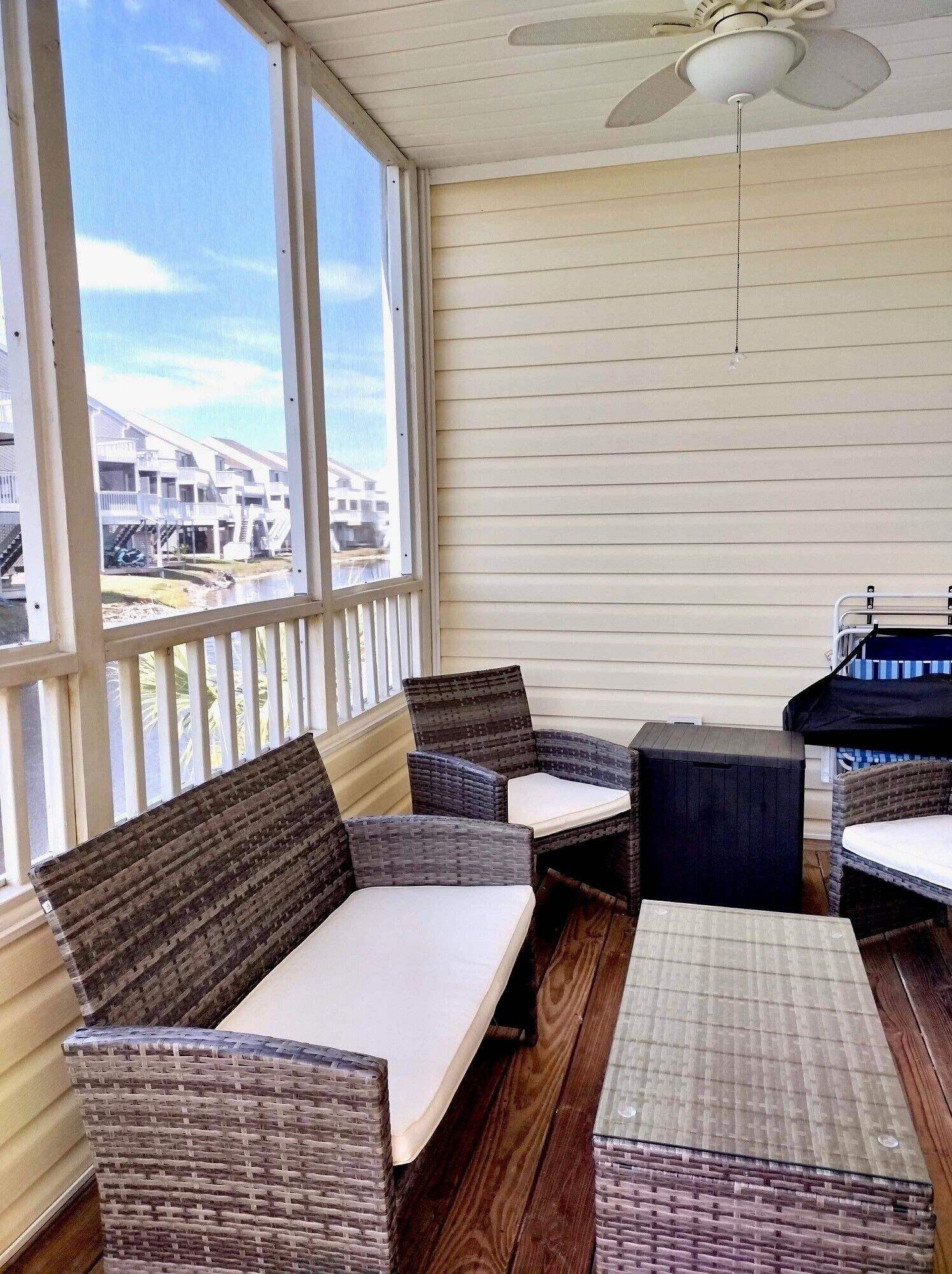 Un patio techado con mobiliario de mimbre, ventanas amplias y un ventilador de techo.