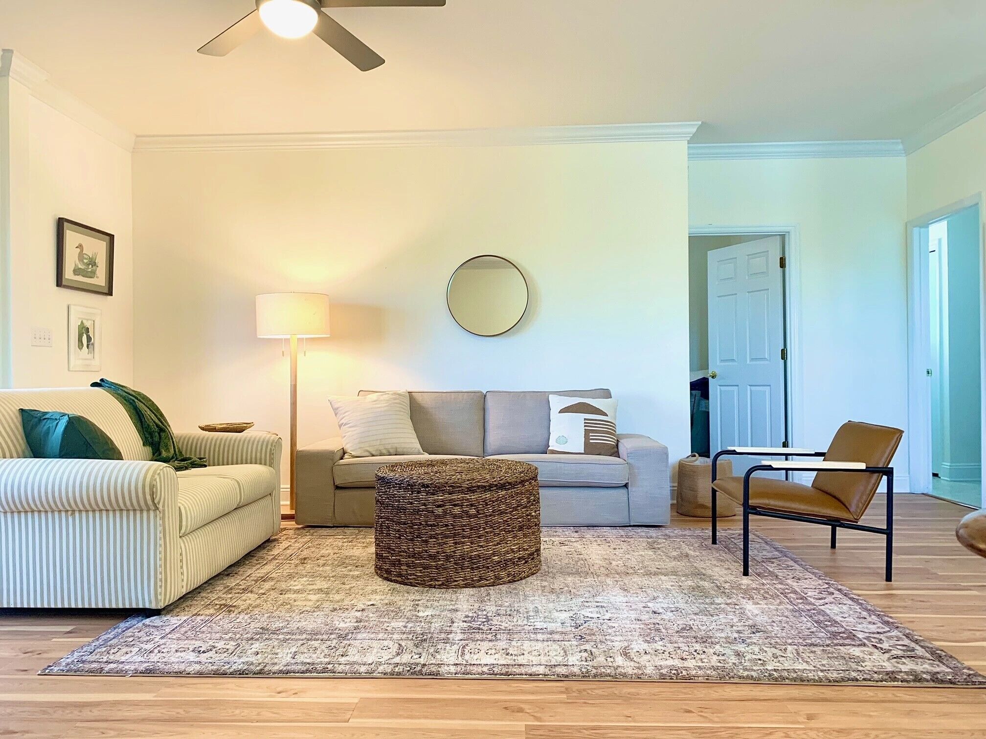 A living room with a sofa, armchair, floor lamp, and a round mirror on the wall.