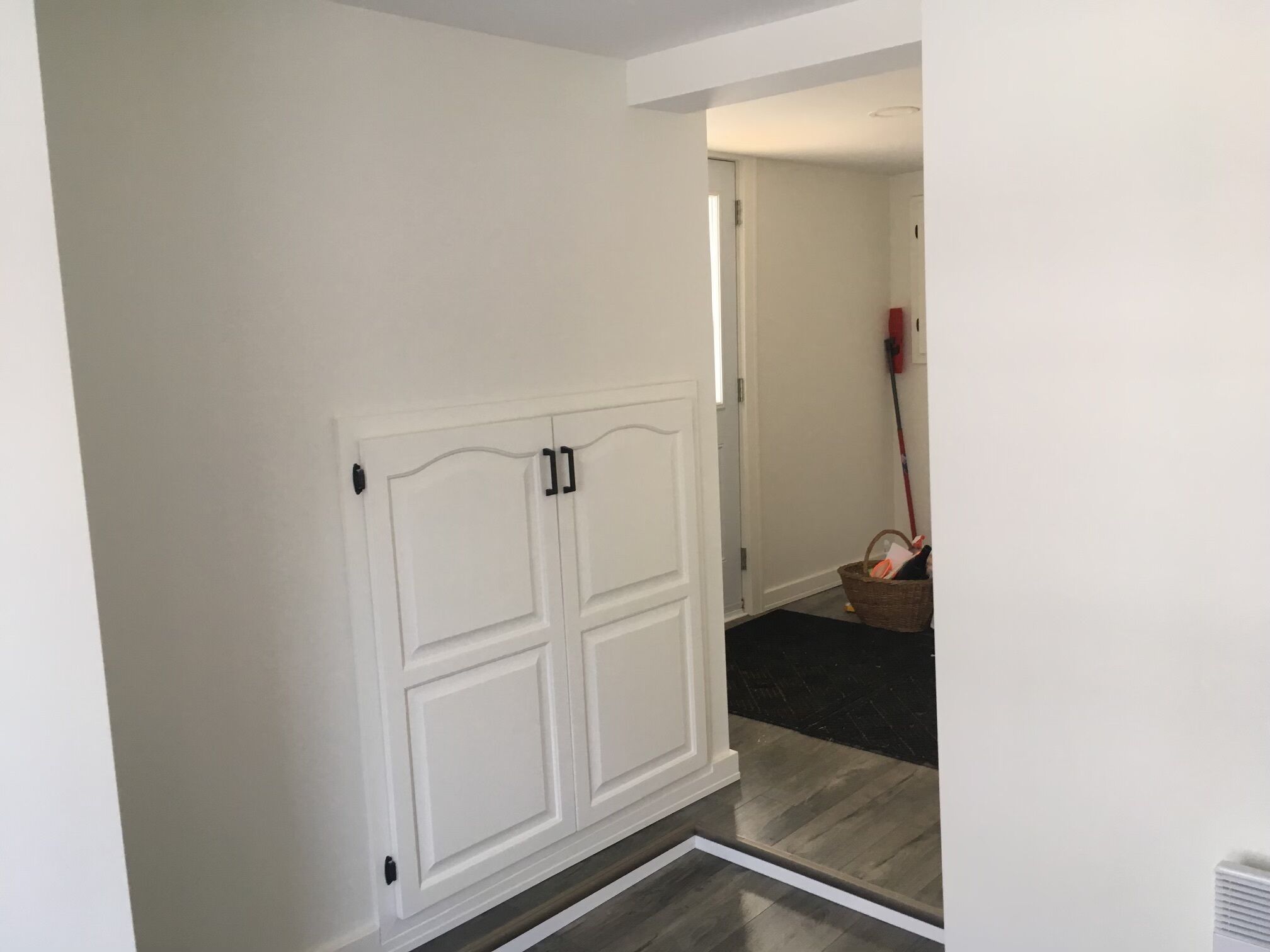 A hallway with a white door, a broom, and a basket.