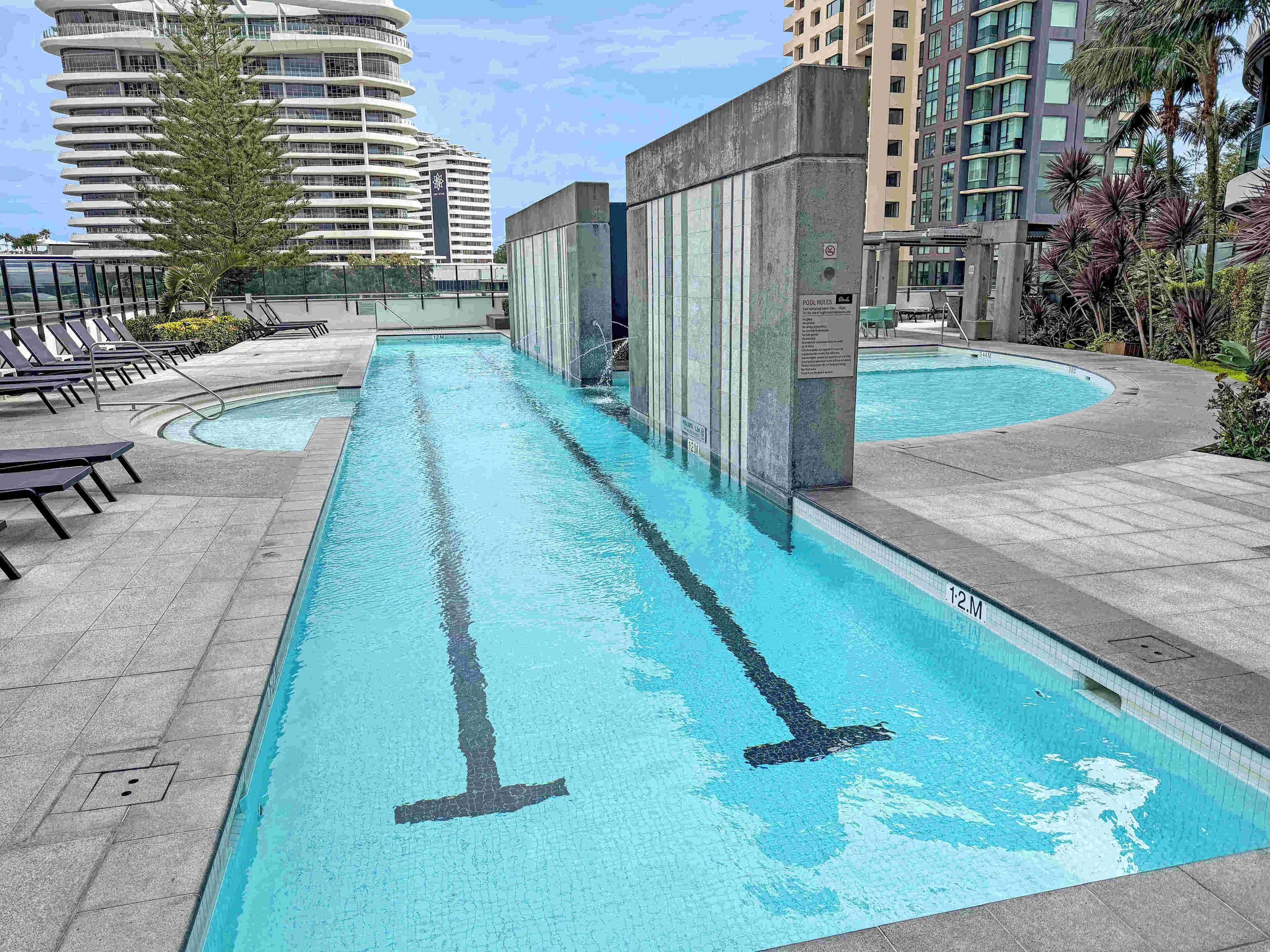 Ein Swimmingpool mit klarer Wasserlinie, umgeben von Liegestühlen und einer Betonmauer mit einem Schild.