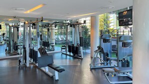 A modern gym with various exercise machines, large windows, and a bench. - Stunning Ocean Views Oracle Level 30 Parking (Broadbeach)