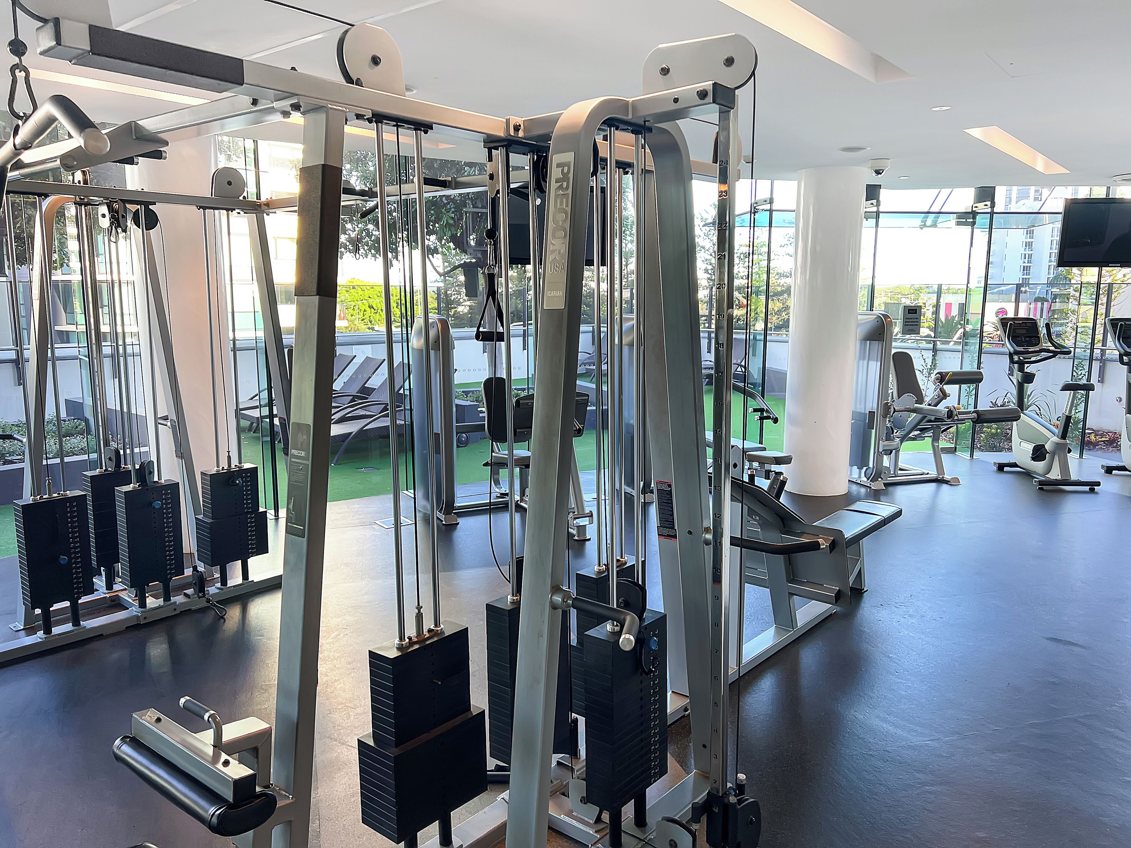 Une salle de sport équipée de divers appareils d’exercice, dotée de grandes fenêtres et offrant une vue sur l’extérieur.