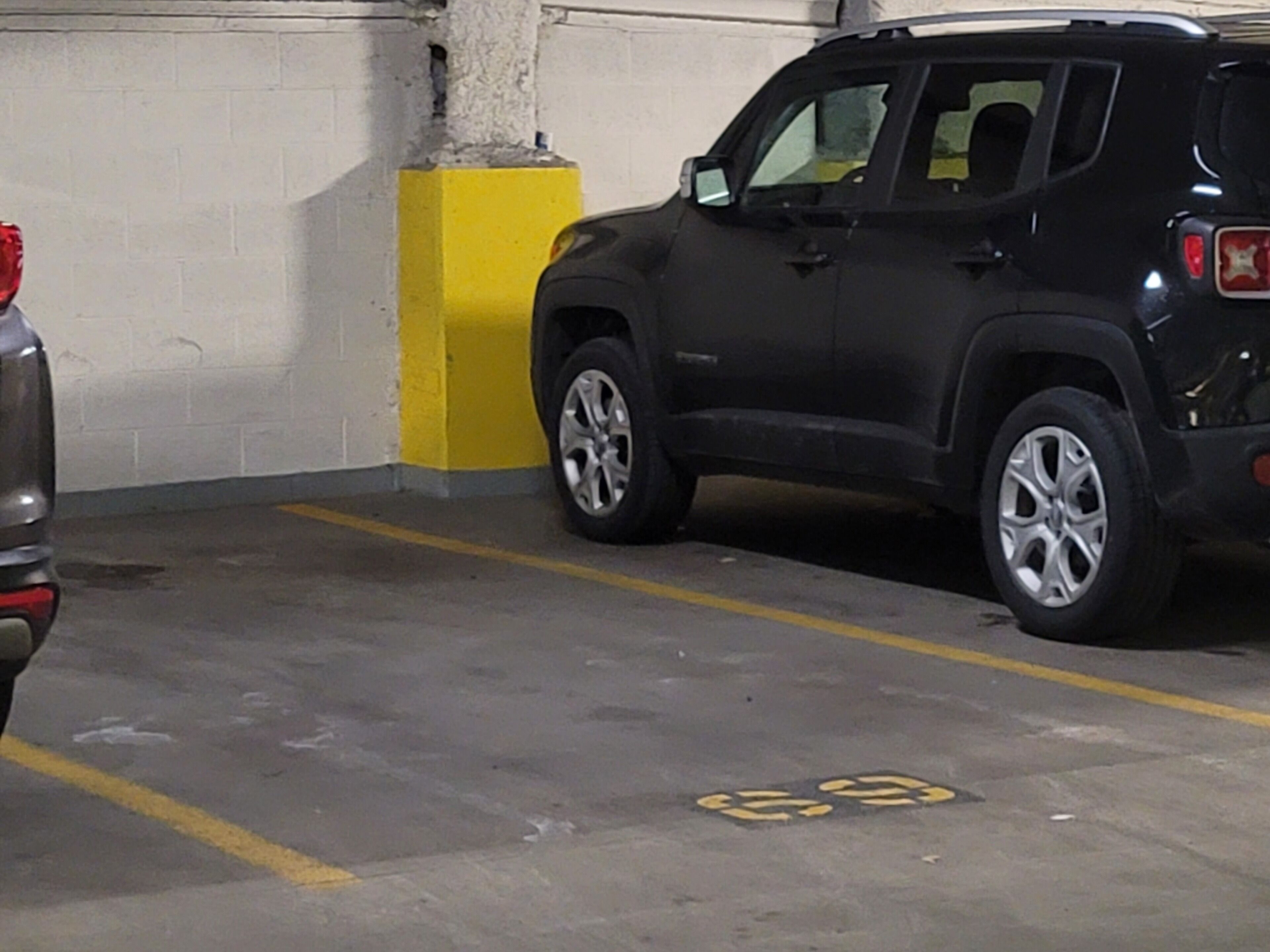 Een parkeergarage met een zwarte SUV naast een gele paal.