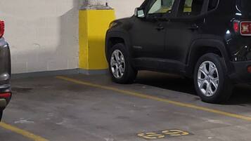 Een parkeergarage met een zwarte SUV naast een gele paal.
