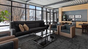 A modern interior with a sofa, chairs, a glass coffee table, and a kitchen area with a grey wall and framed pictures.