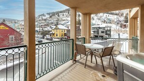Un balcon avec un jacuzzi, des chaises et une vue sur une ville enneigée.