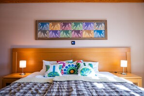 Un letto rifatto con cuscini colorati, una testiera, lampade sui comodini e un quadro incorniciato sopra il letto.