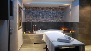 A modern bathroom with a bathtub, a shower area, and a bed with towels.