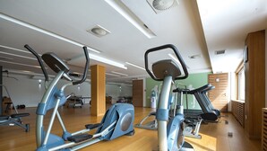 A gym with various exercise machines, wooden flooring, and a large mirror.