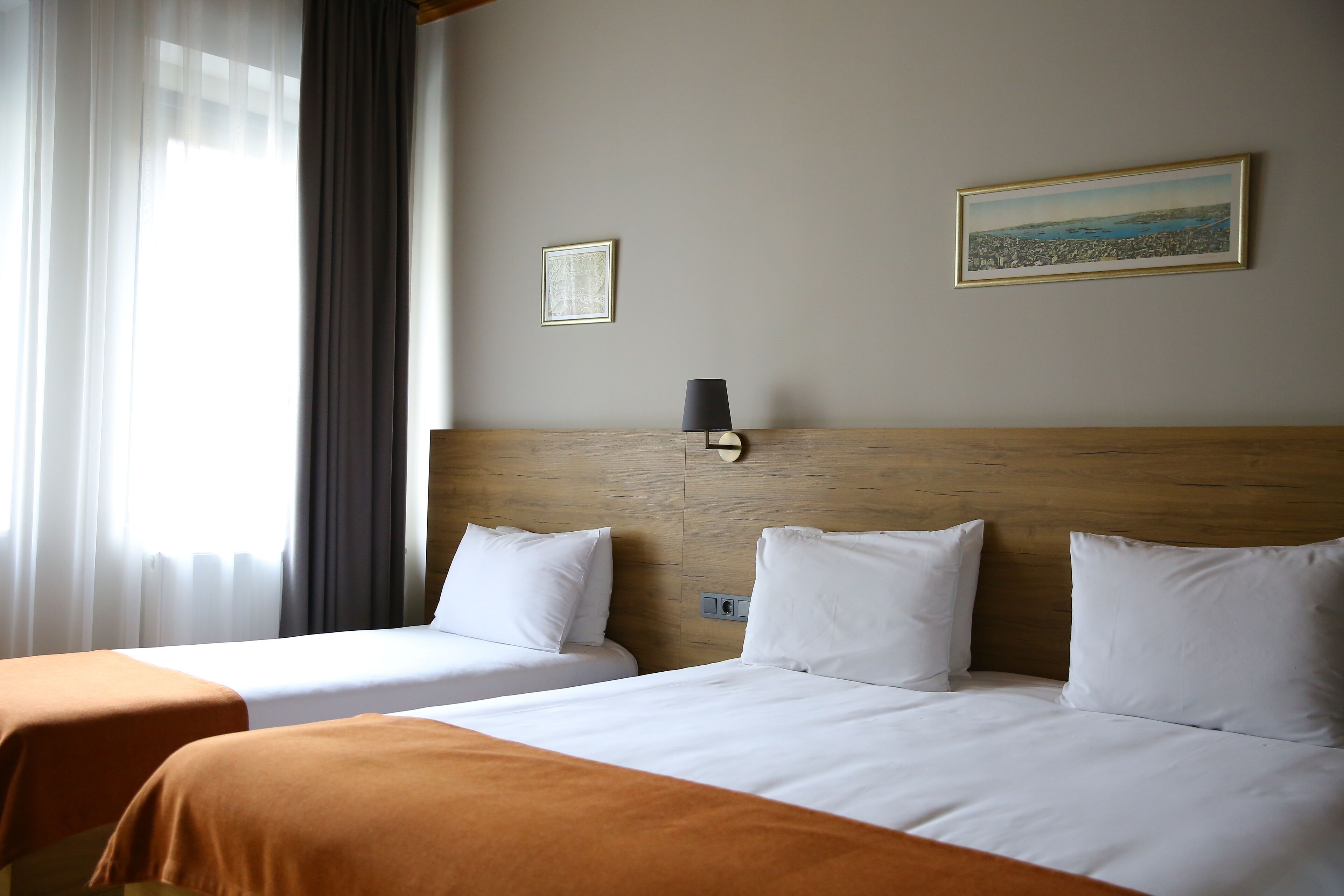 A hotel room with two beds, a wooden headboard, a framed picture, and a lamp.