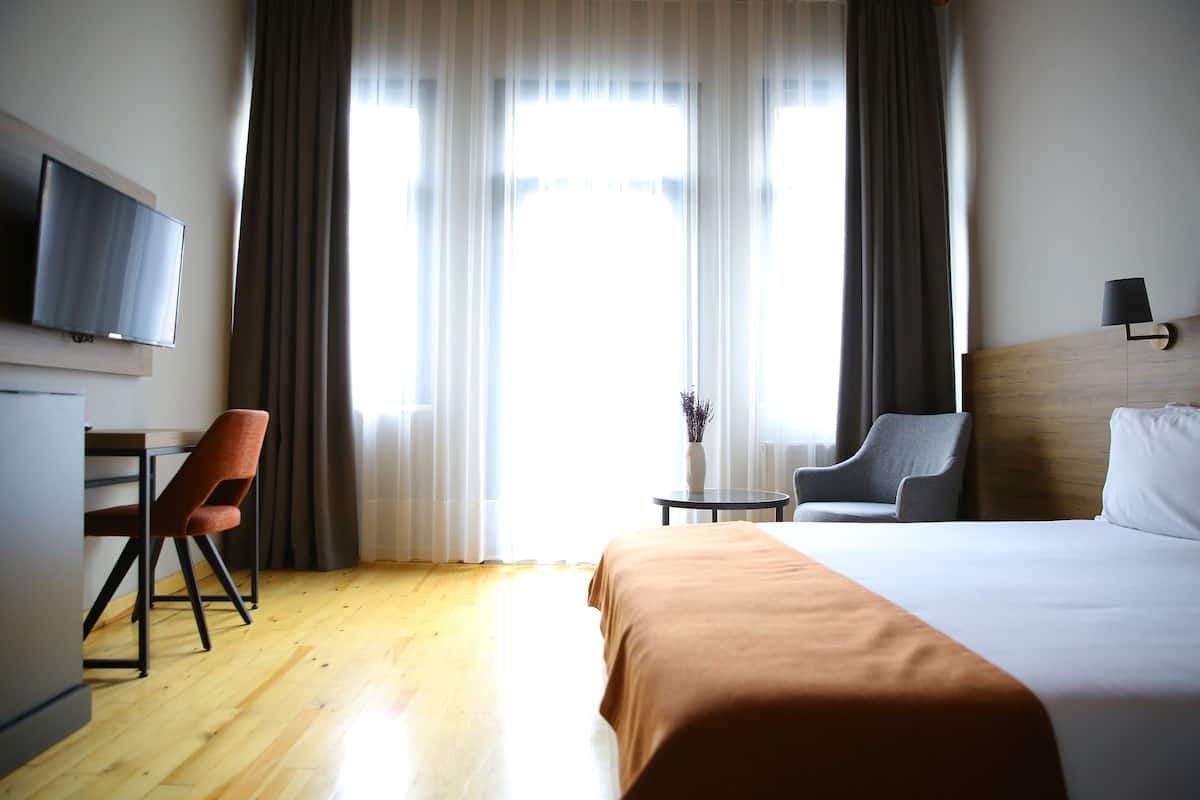 A hotel room with a bed, a desk, a chair, a TV, and a lamp.