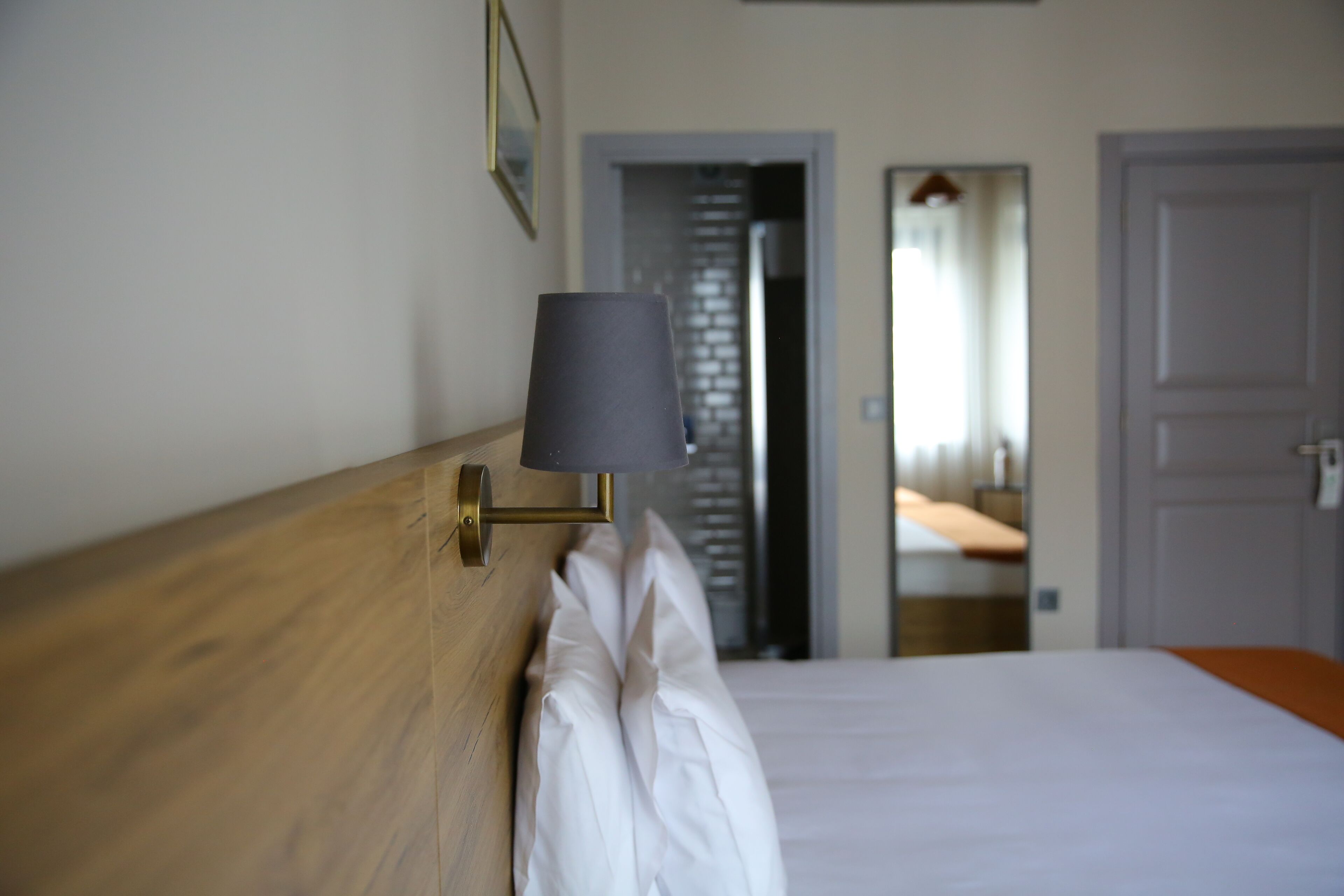 Une chambre d’hôtel avec une tête de lit en bois, une lampe de chevet, du linge de lit blanc et une porte donnant sur une autre pièce.