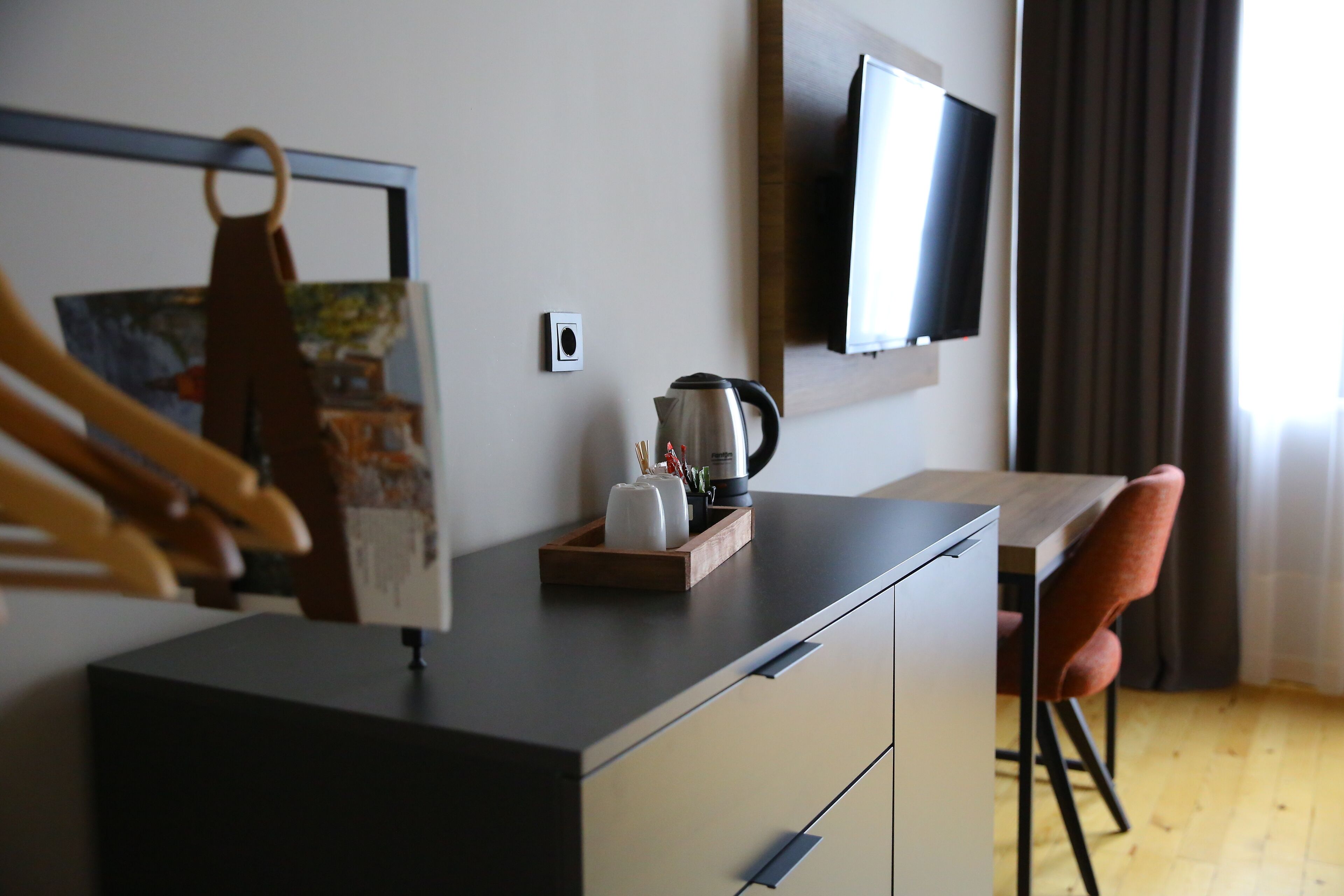A modern hotel room with a wooden desk, a television mounted on the wall, and a chair.