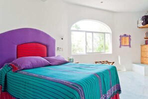 A bedroom with a large bed, a window, and a wooden dresser.