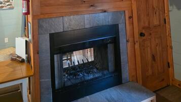 A fireplace with a stone surround, a wooden door to the right, and a small table with a white appliance on it.