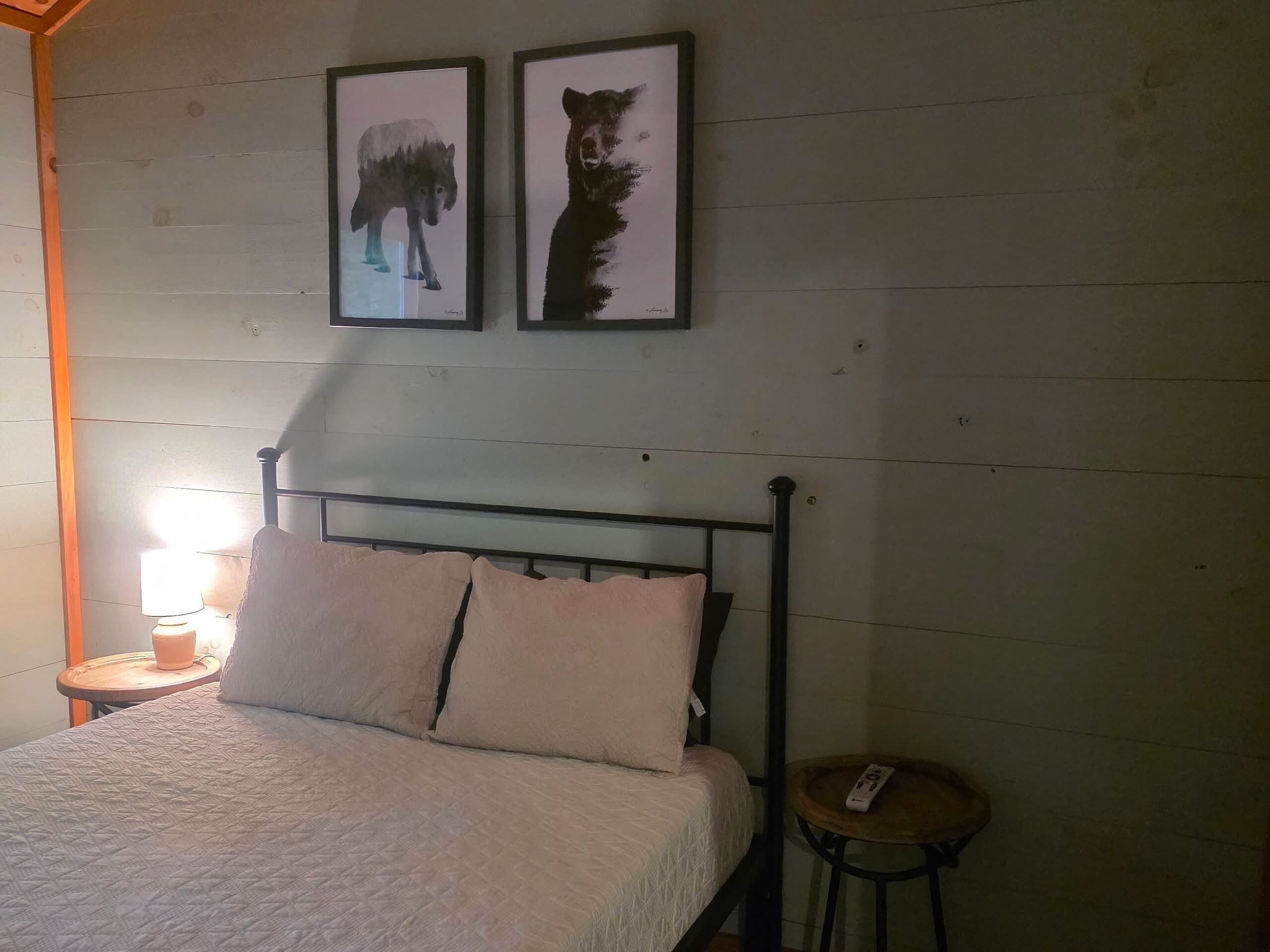 Een kamer met een bed, een nachtkastje, een lamp en twee foto's in lijsten aan de muur.