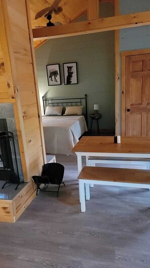 Ein Zimmer mit Holzboden, einem Bett, einem Tisch, einem Stuhl und einem kleinen Tisch mit einer Lampe.