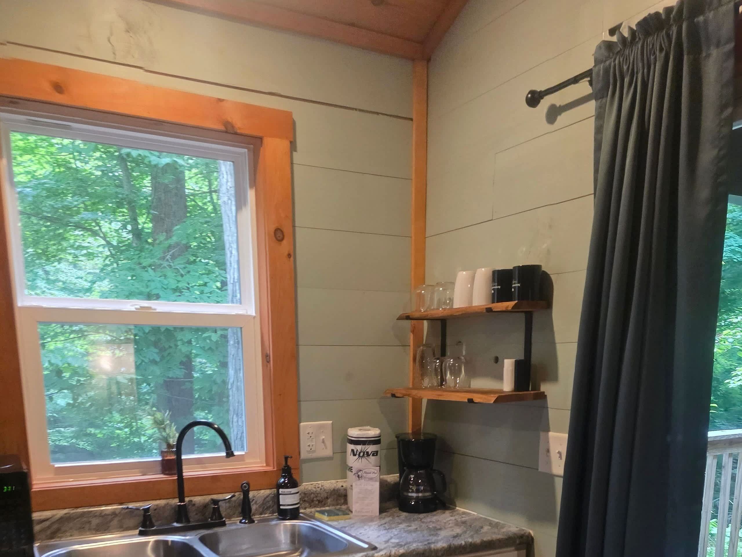 A kitchen with a window, a sink, a coffee maker, and shelves with glassware.