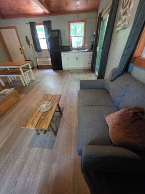 Ein gemütliches Wohnzimmer mit einer Couch, einem Holztisch und einer Küchenzeile mit Schränken und einem Kühlschrank.