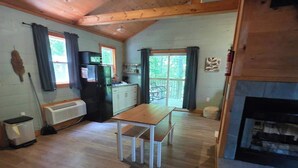 Interior de una cabaña con una mesa de comedor de madera, una zona de cocina, una chimenea y vistas al exterior.