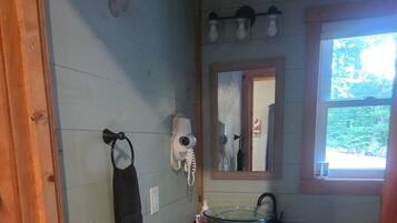 Ein Badezimmer mit einem Waschbecken aus Glas, einem Handtuch auf einem Halter, einem Fön und einem Spiegel über dem Waschbecken.