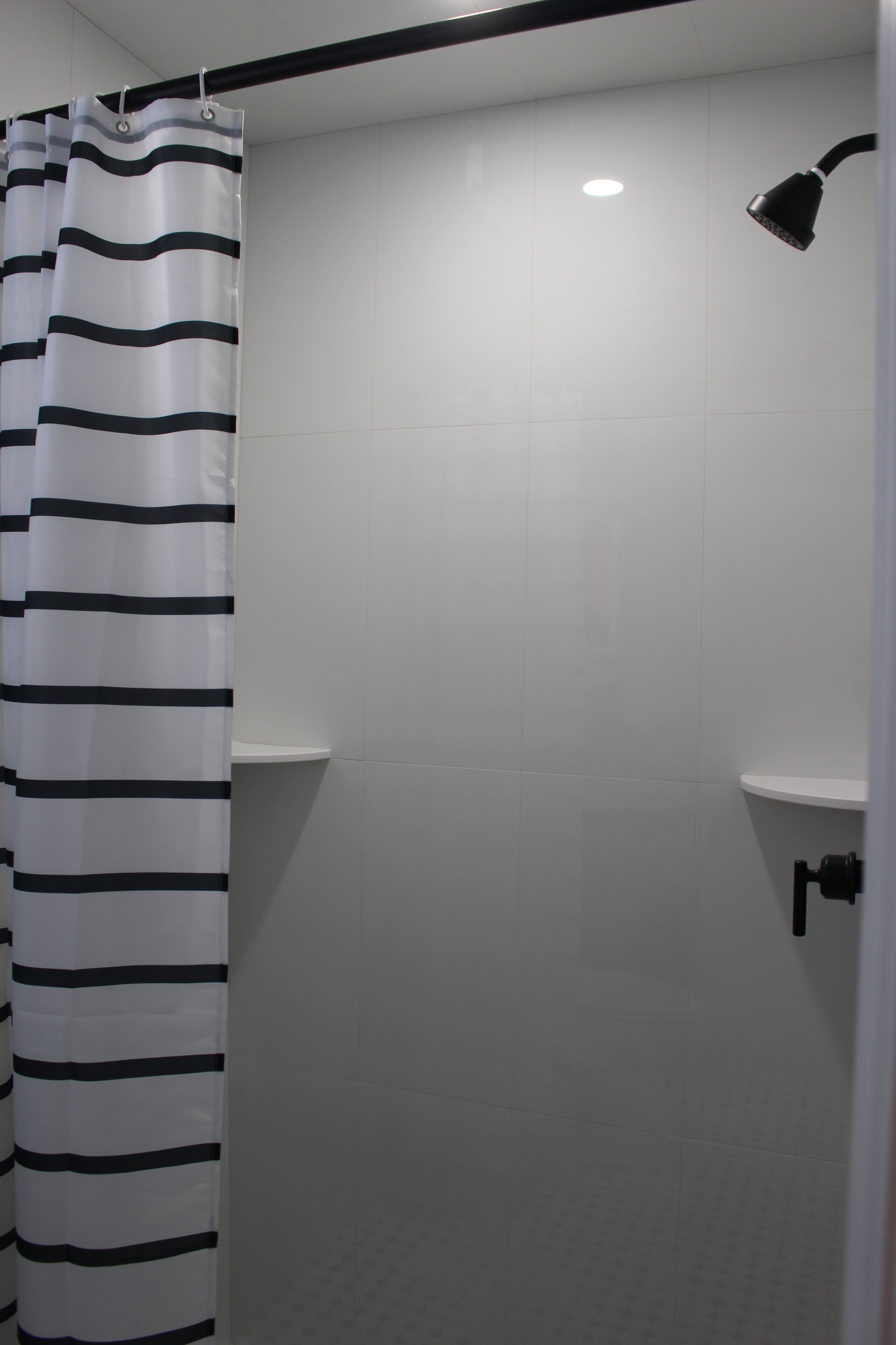 Zona de ducha con cortina de baño a rayas, paredes de azulejos blancos y un cabezal de ducha de mano.