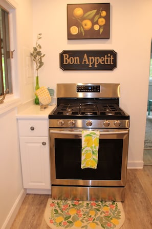 Une cuisine avec un four en acier inoxydable, un meuble blanc, un vase vert et un panneau mural sur lequel on peut lire « Bon appétit ».