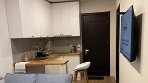 Un espacio habitable compacto con un sofá gris, una mesita blanca y un televisor montado en la pared.