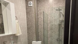Un baño moderno con ducha de vidrio, un lavamanos blanco y un inodoro.