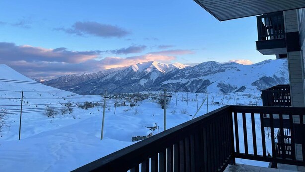 Paisaje montañoso nevado con un telesilla y un edificio de madera con balcón.