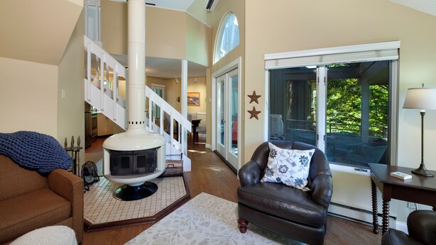 A cozy living room with a fireplace, a leather armchair, and a view of the outdoors through a glass door. - Hawk's Nest 5 (Glen Arbor)