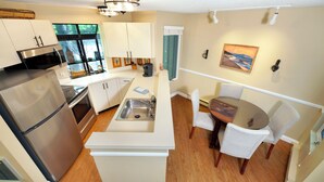 A modern kitchen with a stainless steel refrigerator, a microwave, and a sink. There is a dining area with a table and chairs. - Hawk's Nest 5 (Glen Arbor)