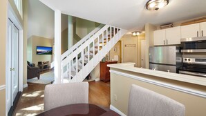 A modern kitchen with a stainless steel refrigerator, a microwave, and a double oven. There is a wooden staircase leading to an upper level. - Hawk's Nest 5 (Glen Arbor)