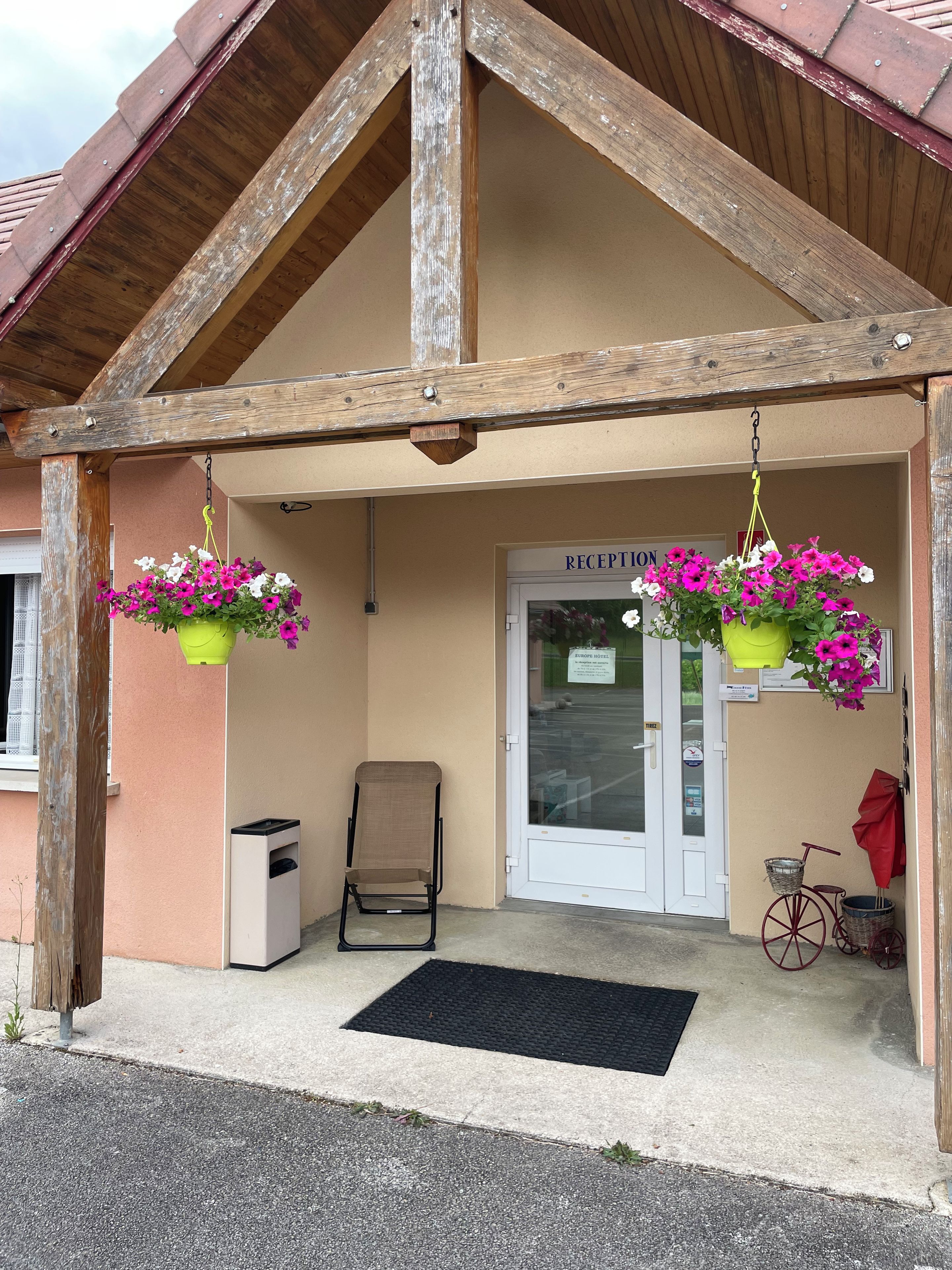 A hotel entrance with a wooden facade, a reception desk, and hanging flower baskets.