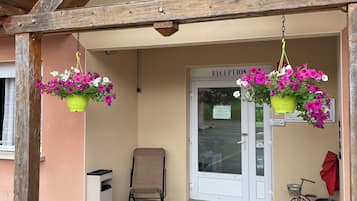 A hotel entrance with a wooden facade, a reception desk, and hanging flower baskets.