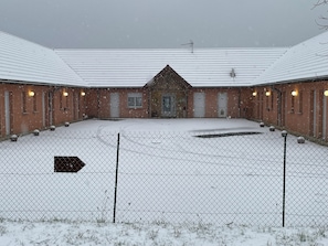 Un patio amurallado con un edificio que presenta varias puertas y ventanas, rodeado de nieve.