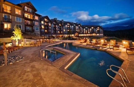 A hotel with a swimming pool, outdoor seating, and a mountainous backdrop.