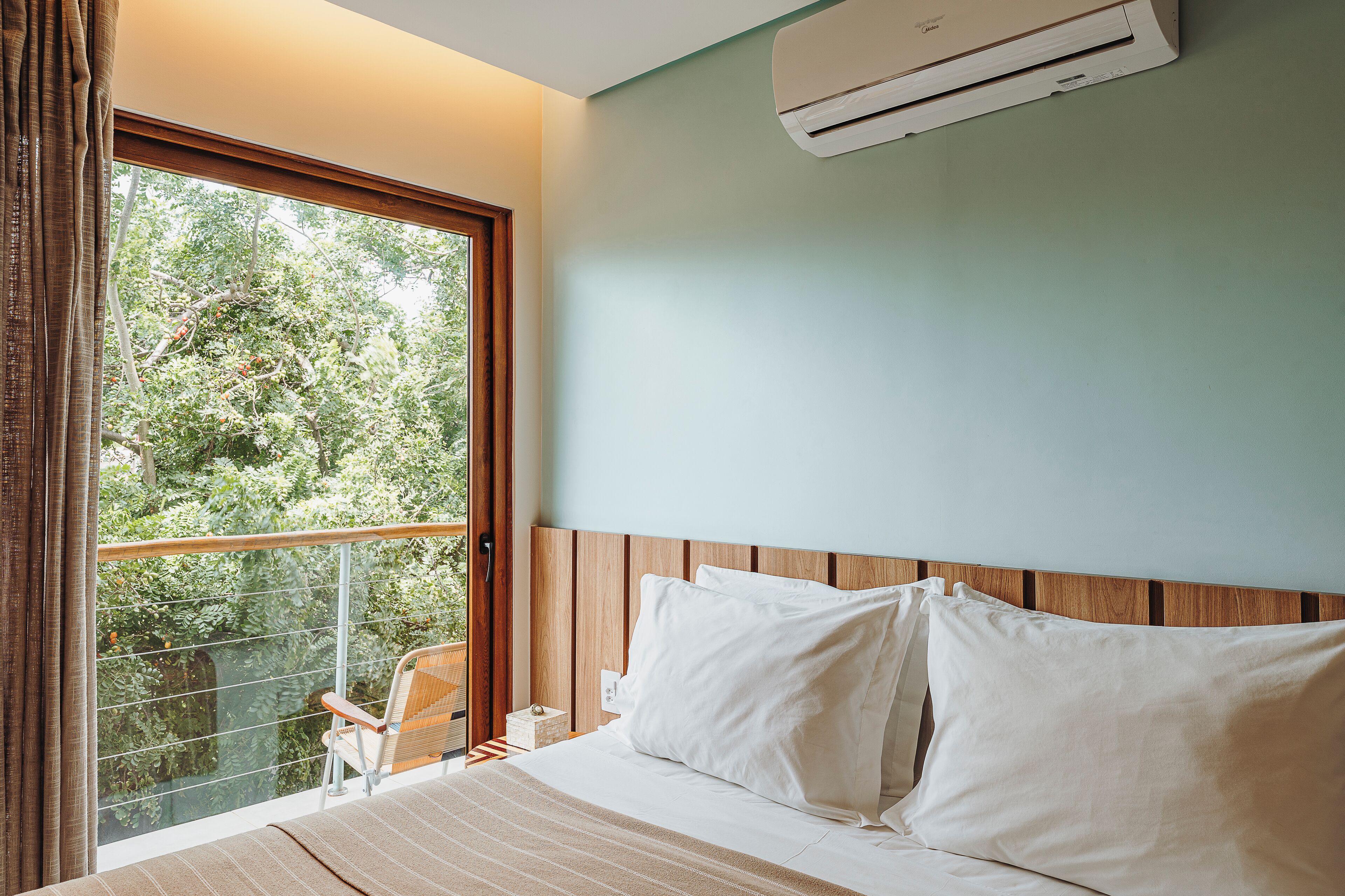 A bedroom with a large window, a bed with white linens, and an air conditioning unit on the wall.