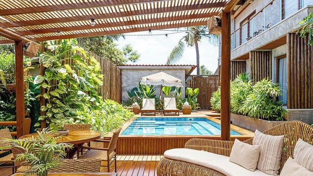 A poolside area with a wooden deck, wicker furniture, and lush greenery. -  Vila Sal Boutique Noronha (Fernando de Noronha)