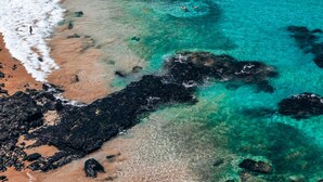 An aerial view of a beach with clear turquoise waters, a sandy shore, and rocky outcrops. -  Vila Sal Boutique Noronha (Fernando de Noronha)