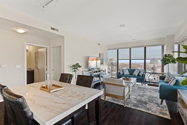 A modern living room with a dining area, large windows, and a view of the city.