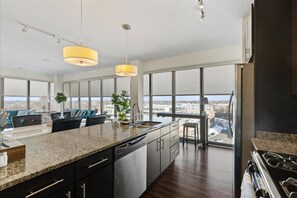 A modern kitchen with a large island, stainless steel appliances, and a view of the city through large windows.