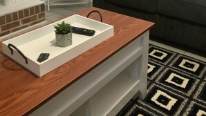 Een woonkamer met een donkergrijze bank, een witte bijzettafel met een afstandsbediening, een zwarte handdoek, een kunstwerk in een lijst en een bordje met de tekst 'RELAX'.